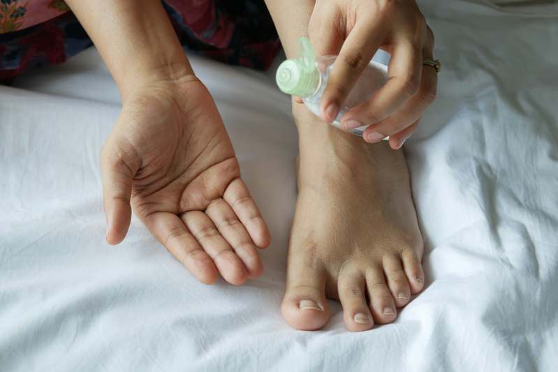 Close-up of hands gently massaging foot cream onto clean feet, with natural light and wooden textures in the background